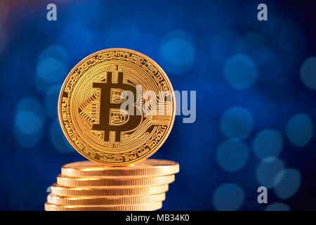 Pila di golden bitcoins con uno bitcoin sul suo bordo collocata su sfocato sfondo blu. Digital denaro virtuale blockchain stock exchange futuro finanziamento bancario innovative web business Foto Stock