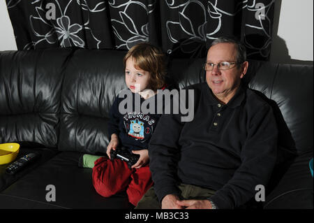 Un giovane ragazzo mantiene un controllo playstation mentre concentrando sul gioco seduto accanto a suo nonno come egli guarda a. Foto Stock