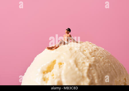 Un uomo in miniatura che indossano il costume da bagno rilassante per un gelato sfera, contro un sfondo rosa con qualche spazio vuoto sulla parte superiore Foto Stock