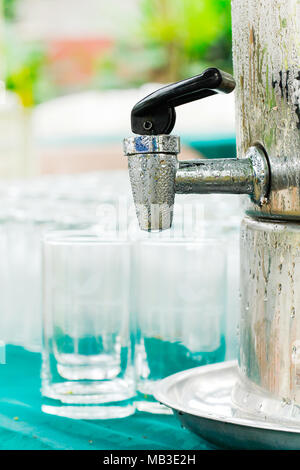 Una gocciolina d'acqua in acciaio inox con un bicchiere di acqua sul tavolo. Foto Stock