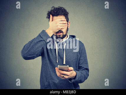 Triste spiacevoli giovane con il telefono cellulare che copre con la mano il suo volto Foto Stock