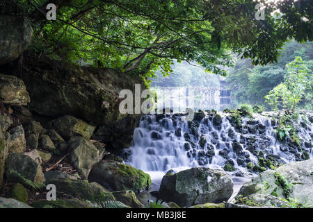 Una piccola cascata con pietre e rocce enormi a Chonjiyeon, una lunga esposizione, Seogwipo, Jeju Island, Corea del Sud Foto Stock