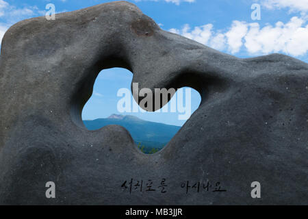 Top cratere del monte hallasan vulcano visto attraverso una scultura in pietra in una giornata di sole in un parco di Seogwipo, Jeju Island, Corea Foto Stock