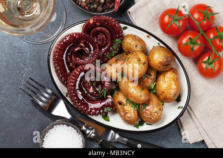 Polpo alla griglia con patate piccole con erbe e spezie e vino bianco in vetro. Vista superiore Foto Stock