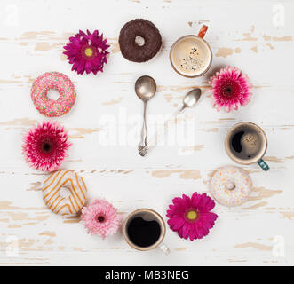 Tazza da caffè, ciambelle e gerbera Orologio dei fiori di colore bianco su un tavolo di legno. Vista superiore Foto Stock