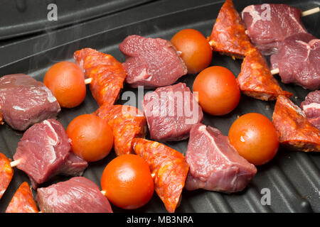 Il cinghiale spiedini, il salame chorizo e pomodori ciliegia appena iniziando a cuocere a George Foreman grill. La carne di cinghiale è più scuro di quello interno e di maiale Foto Stock