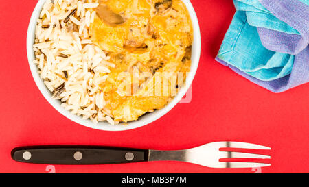 Pollo e funghi Stroganoff con riso contro uno sfondo rosso Foto Stock