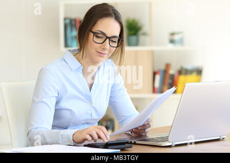 Donna che indossa occhiali lavorando il calcolo con una calcolatrice a casa Foto Stock