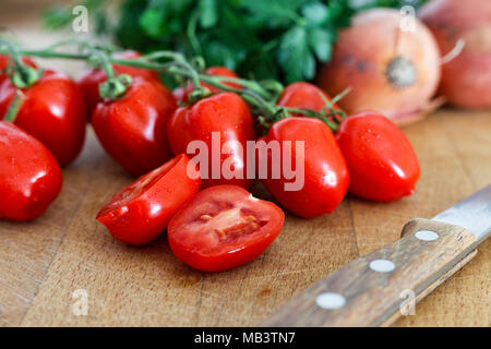Pomodori uva sulla vite con uno dimezzato il pomodoro su legno tagliere accanto a un coltello da cucina. Foto Stock