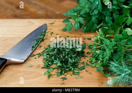 Fresco tritato fino mazzetto di prezzemolo su legno tagliere accanto al coltello da cucina. Foto Stock