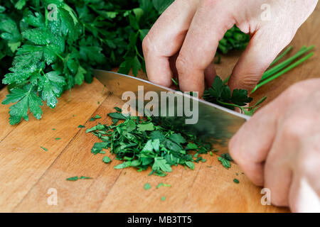 Dettaglio delle mani sminuzzare un mazzetto di prezzemolo su legno tagliere con un coltello da cucina. Foto Stock