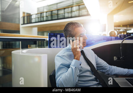 Focalizzato imprenditore maturo in una camicia e cravatta seduti ad un armadio in un moderno edificio per uffici a parlare su un telefono cellulare Foto Stock