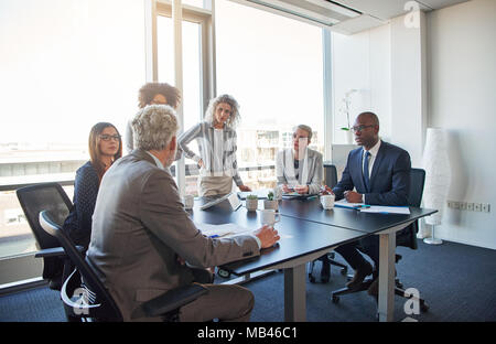 Diversi gruppi di dirigenti a discutere di affari insieme attorno ad un tavolo durante una riunione in un luminoso ufficio moderno Foto Stock