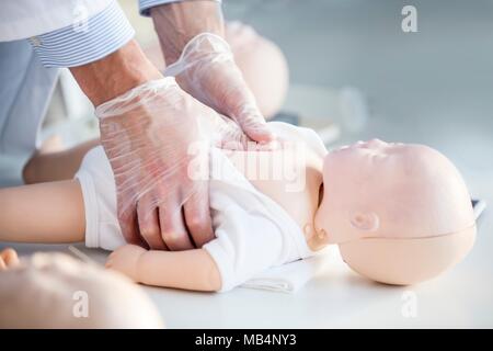 Medico esercitarsi compressioni toraciche su un neonato CPR manichino di formazione. Foto Stock