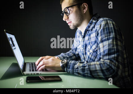 Giovane uomo che lavora sul computer di notte nel buio ufficio. Il designer lavora in un tempo successivo. Un giovane uomo si siede davanti al computer Foto Stock