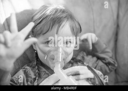 Bambina in una maschera, trattamenti del tratto respiratorio con un nebulizzatore a casa Foto Stock