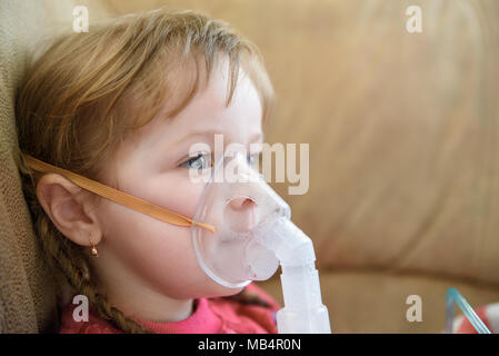 Bambina in una maschera, trattamenti del tratto respiratorio con un nebulizzatore a casa Foto Stock