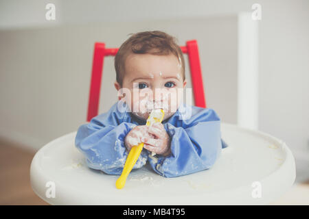 Bambino di 6 mesi boy alimentare se stesso yogurt con un cucchiaio Foto Stock