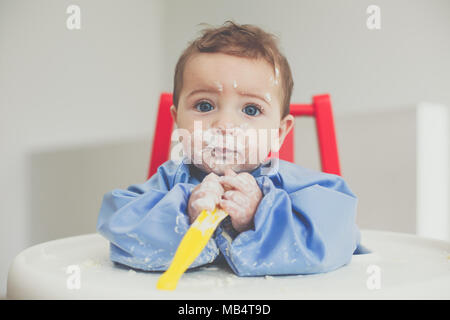 Bambino di 6 mesi boy alimentare se stesso yogurt con un cucchiaio Foto Stock