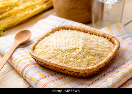 Non cotti riso basmati, extra lunghi tipo, in una piastrina su un asciugamano messo su un tavolo di legno. Il riso Basmati è un ingrediente di base per molti orientali Asiatici Foto Stock