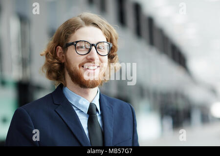 Giovani sorridente barbuto imprenditore nel convenzionale guardando la telecamera all'interno di edificio moderno Foto Stock