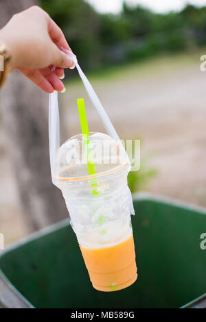Non dimenticatevi di gettare il vostro cestino nel cestino. Donna di mano è di gettare il bicchiere vuoto per un verde bin, una tazza di plastica di Thai tè, Foto Stock