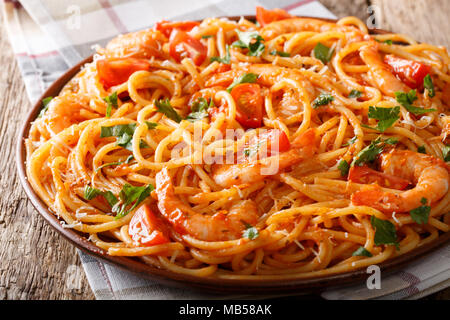 La pasta italiana spaghetti con gamberi e parmigiano ed erbe nel pomodoro salsa diavolo close-up su una piastra orizzontale. Foto Stock