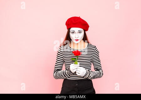 Ritratto di donna carina tenendo una rosa rossa. Clown, artista , mime. Studio shot, sfondo rosa Foto Stock