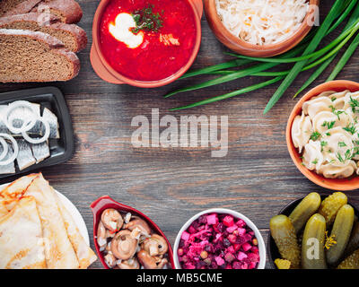 Cibo russo su sfondo di legno. Assortimento di piatti della cucina russa - borscht, pelmeni, aringhe marinate, funghi, salate cetrioli, condimento, crauti e pancakes. Vista dall'alto. Copia dello spazio. Foto Stock