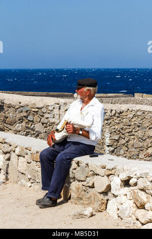 Il vecchio uomo seduto sul muro con cornamuse, Mykonos, Grecia Foto Stock