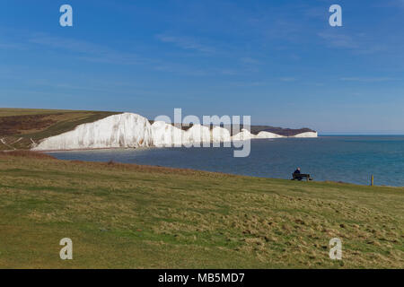 SEAFORD, SUSSEX/UK - Aprile 5 : uomo seduto su una panchina guarda le sette sorelle vicino a Seaford nel Sussex il 5 aprile 2018. Unidentified Man. Foto Stock