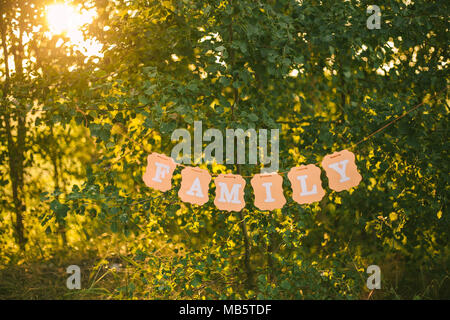 Famiglia di parola scritta su pensile carta arancione banner appesi sugli alberi al di fuori al tramonto o l'alba di tempo. Orizzontale fotografia a colori. Foto Stock