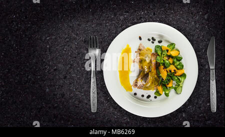 Gambe d'anatra con salsa di arancio e la valeriana con insalata di arance e aceto sulla piastra bianca sul ripiano in granito. Foto Stock