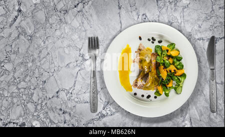 Gambe d'anatra con salsa di arancio e la valeriana con insalata di arance e aceto sulla piastra bianca sul bancone di marmo alto. Foto Stock