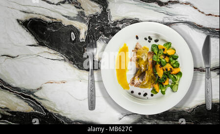 Gambe d'anatra con salsa di arancio e la valeriana con insalata di arance e aceto sulla piastra bianca sul ripiano in granito. Foto Stock