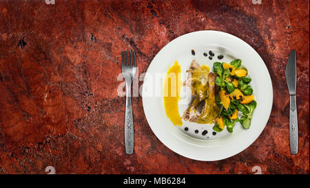 Gambe d'anatra con salsa di arancio e la valeriana con insalata di arance e aceto sulla piastra bianca sul ripiano in granito. Foto Stock