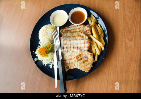 Bistecca di carne di maiale servito con salsa di pomodoro e patate fritte e verdure e riso fritto sulla piastra nel ristorante della Thailandia Foto Stock