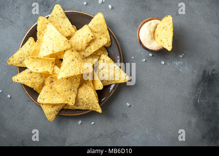 Nachos chips e formaggio fuso. Tortilla di mais nachos messicani chip nella ciotola e salsa al formaggio dip sulla pietra grigia sfondo, copia dello spazio. Foto Stock