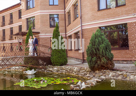 Bello lo sposo e la sposa camminando sul ponte in prossimità di casa di mattoni Foto Stock