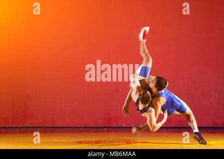 Due greco-romane lottatori in uniforme blu wrestling su un giallo tappeto di wrestling in palestra Foto Stock