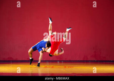 Due greco-romane lottatori in uniforme blu wrestling su un giallo tappeto di wrestling in palestra Foto Stock