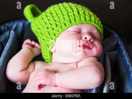 La nostra settimana vecchio figlia addormentato veloce nella mia fotocamera borsa indossando un cappello rane. Foto Stock