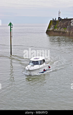 Una piccola barca ritorna alla sicurezza di Porthcawl Marina dopo una giornata di pesca nel canale di Bristol con pescatori sul molo dietro. Foto Stock