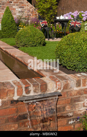 Cascata di acqua dal ruscello, prato, box sfere & Tè per due nella soleggiata " è un riflesso della vita' show garden - RHS Flower Show, Tatton Park, Inghilterra, Regno Unito. Foto Stock