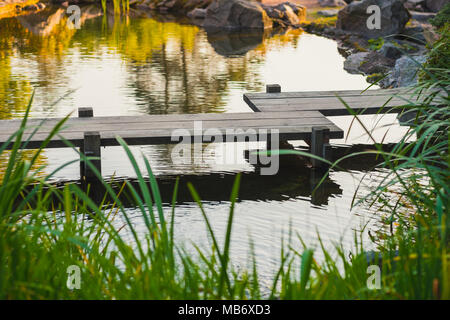 Ponte di legno in stile giapponese su un laghetto in giardino Foto Stock