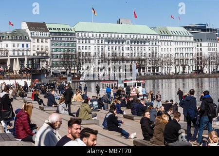 06 aprile 2018, Germania Amburgo: residenti di Amburgo e i turisti che si godono il sole di mezzogiorno di fronte all'hotel di lusso "Vier Jahreszeiten' (lit. Quattro Stagioni) a Jungfernstieg. Foto: Markus Scholz/dpa Foto Stock