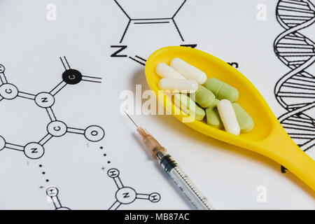 Assortimento di pillole, compresse e capsule in giallo cucchiaio, siringa su sfondo bianco con formula chimica. Foto Stock
