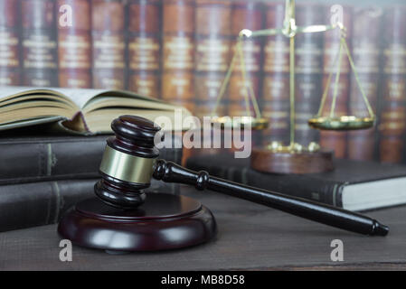 Martello di legno, soundblock, bilance e aprire il vecchio libro contro lo sfondo di una fila di libri antichi e rilegato in pelle Foto Stock