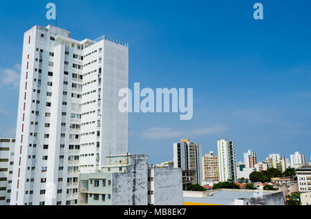 Grande edificio bianco e pieno di finestre in primo piano e sullo sfondo di molti edifici e una grande, pulito cielo blu. Foto Stock