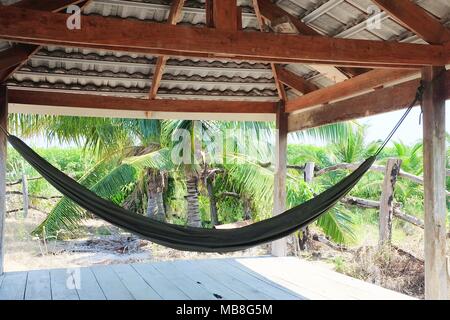 Concetto di rilassamento, l'amaca appesa in cocco Palm Garden. Una imbracatura in tessuto sospeso tra due pali utilizzati per oscillazione, dormire o di riposo Foto Stock